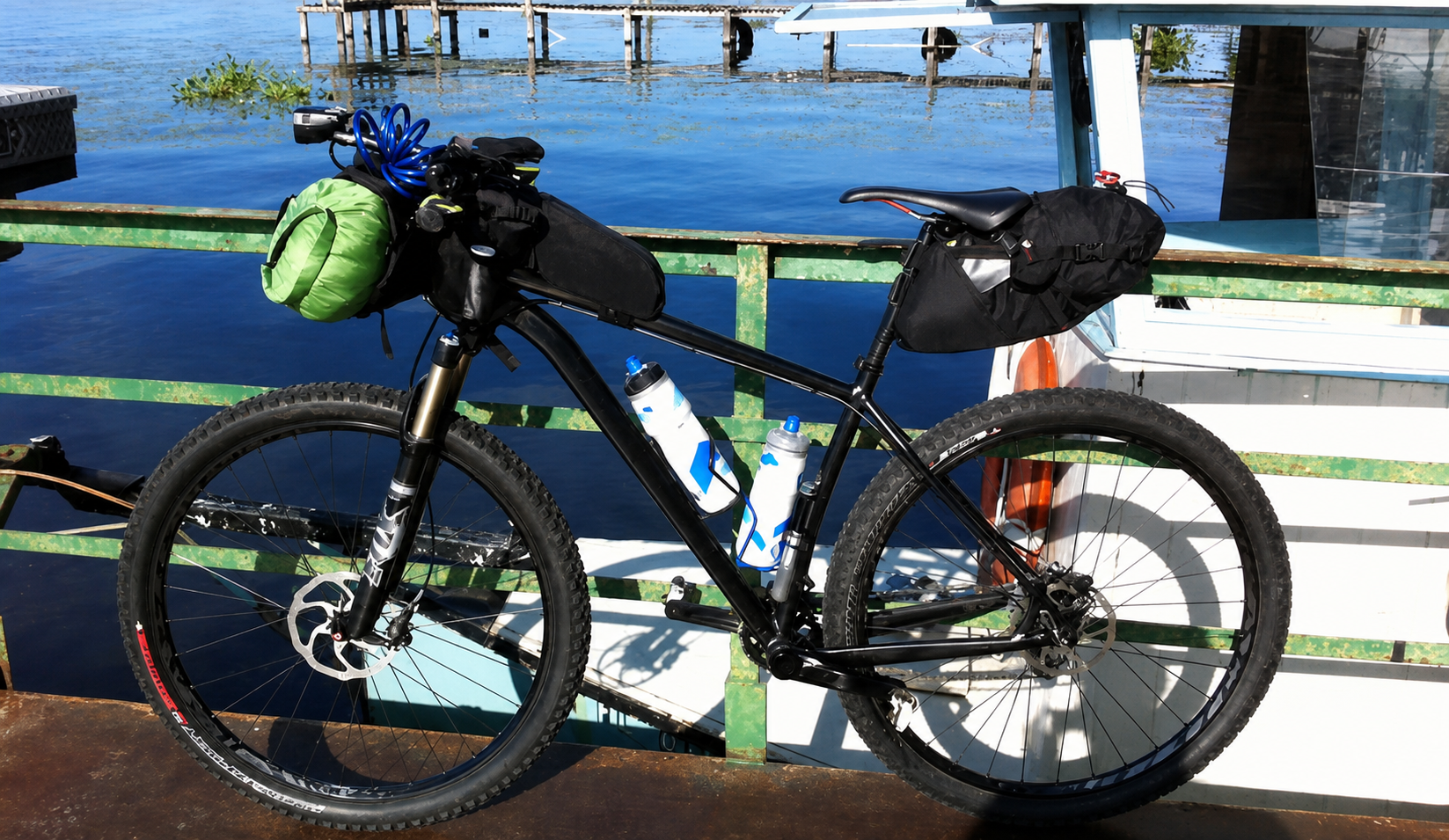 Loaded black mountain bike with frame, seat, and green handlebar bags on the Fort Gates Ferry
